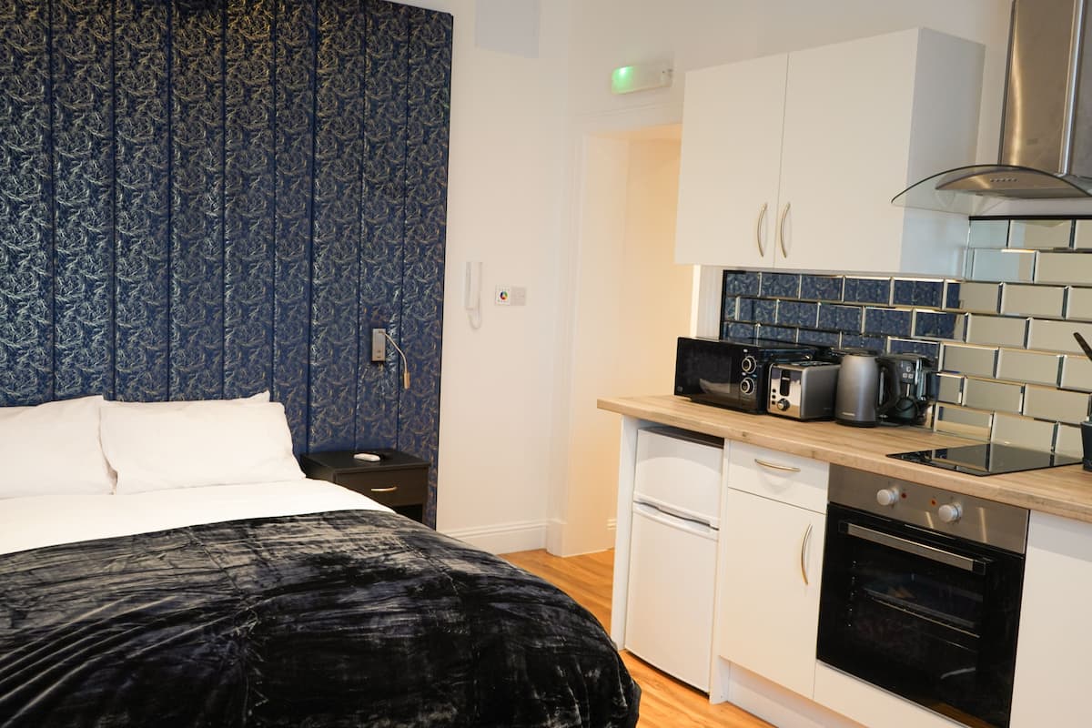 Un dormitorio con cama, mesita de noche y una pequeña kitchenette equipada con microondas, tostadora y horno.
