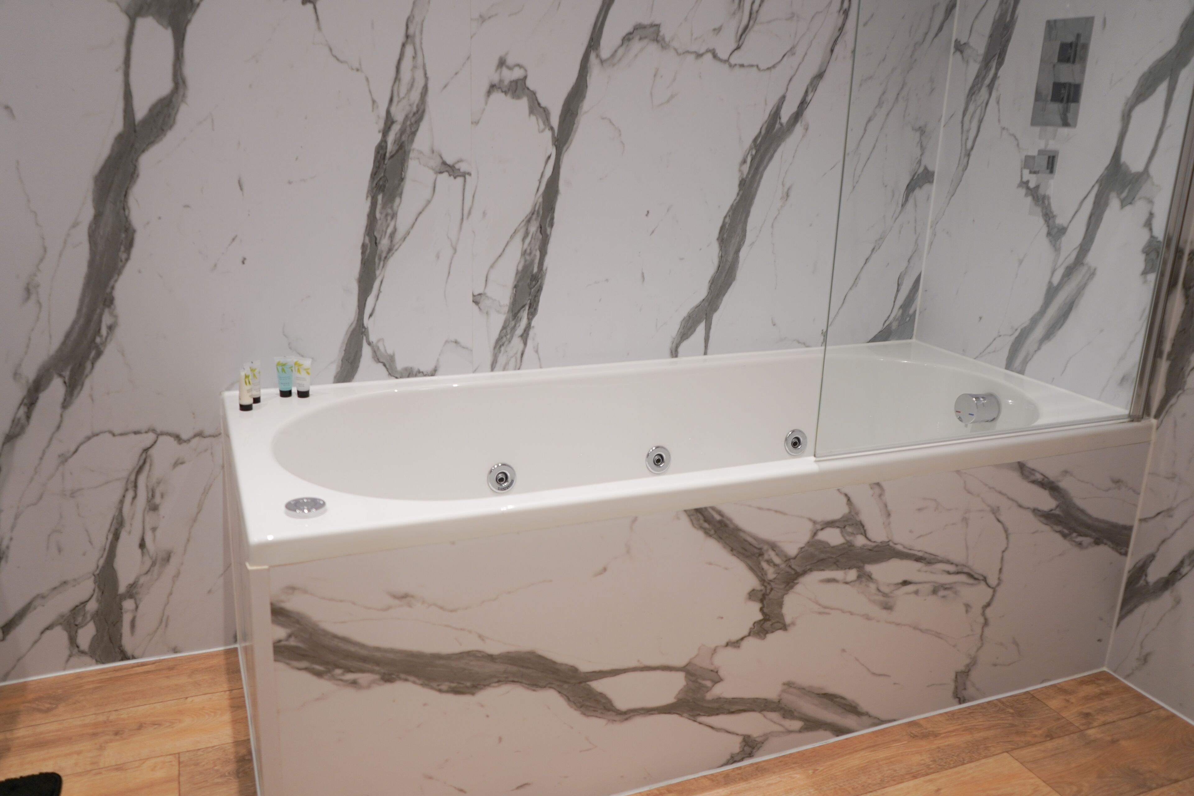 Ein modernes Badezimmer mit Marmorwänden und -boden, einer weißen Badewanne und Holzboden.