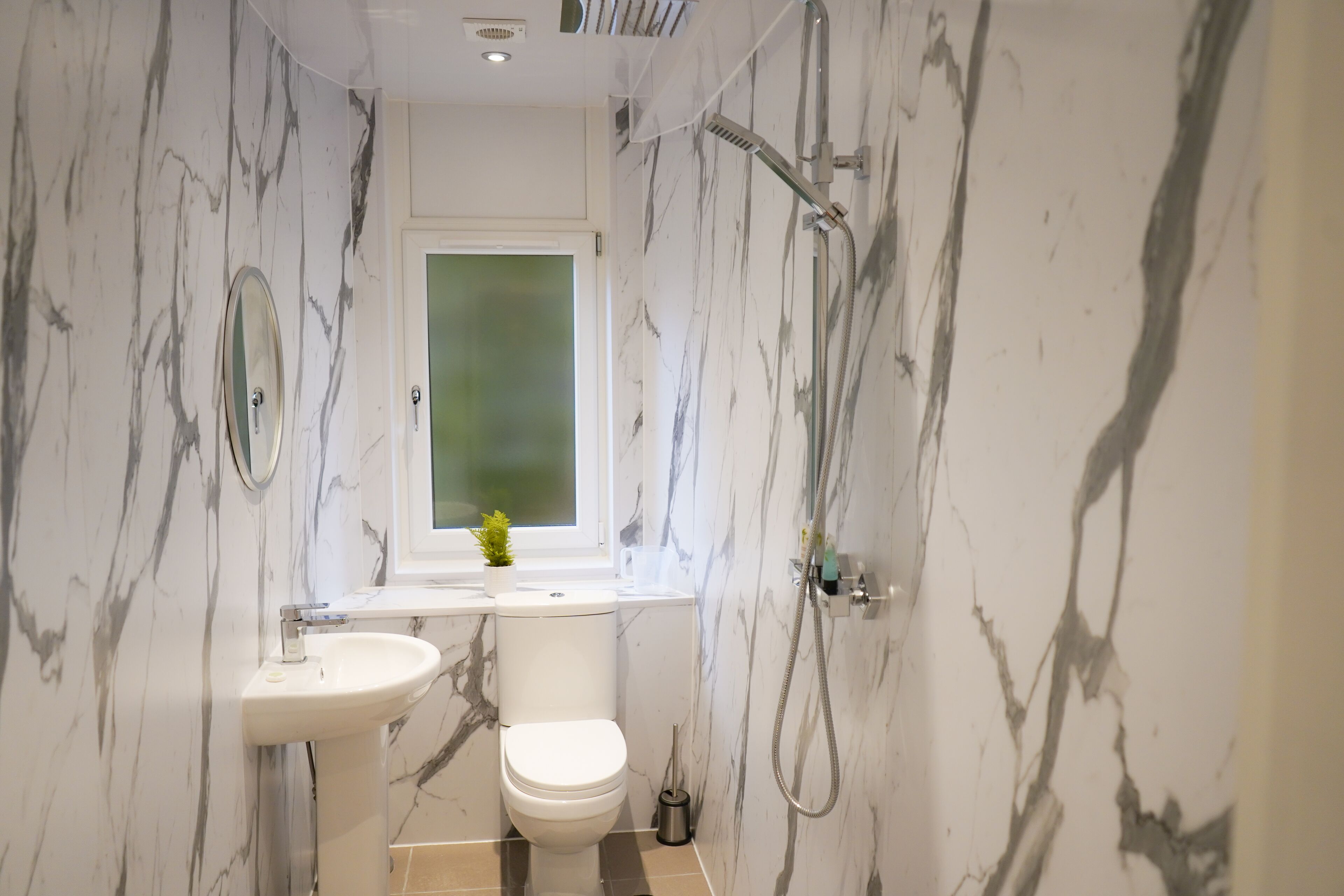 A bathroom with a marble wall, a toilet, a sink, and a shower.