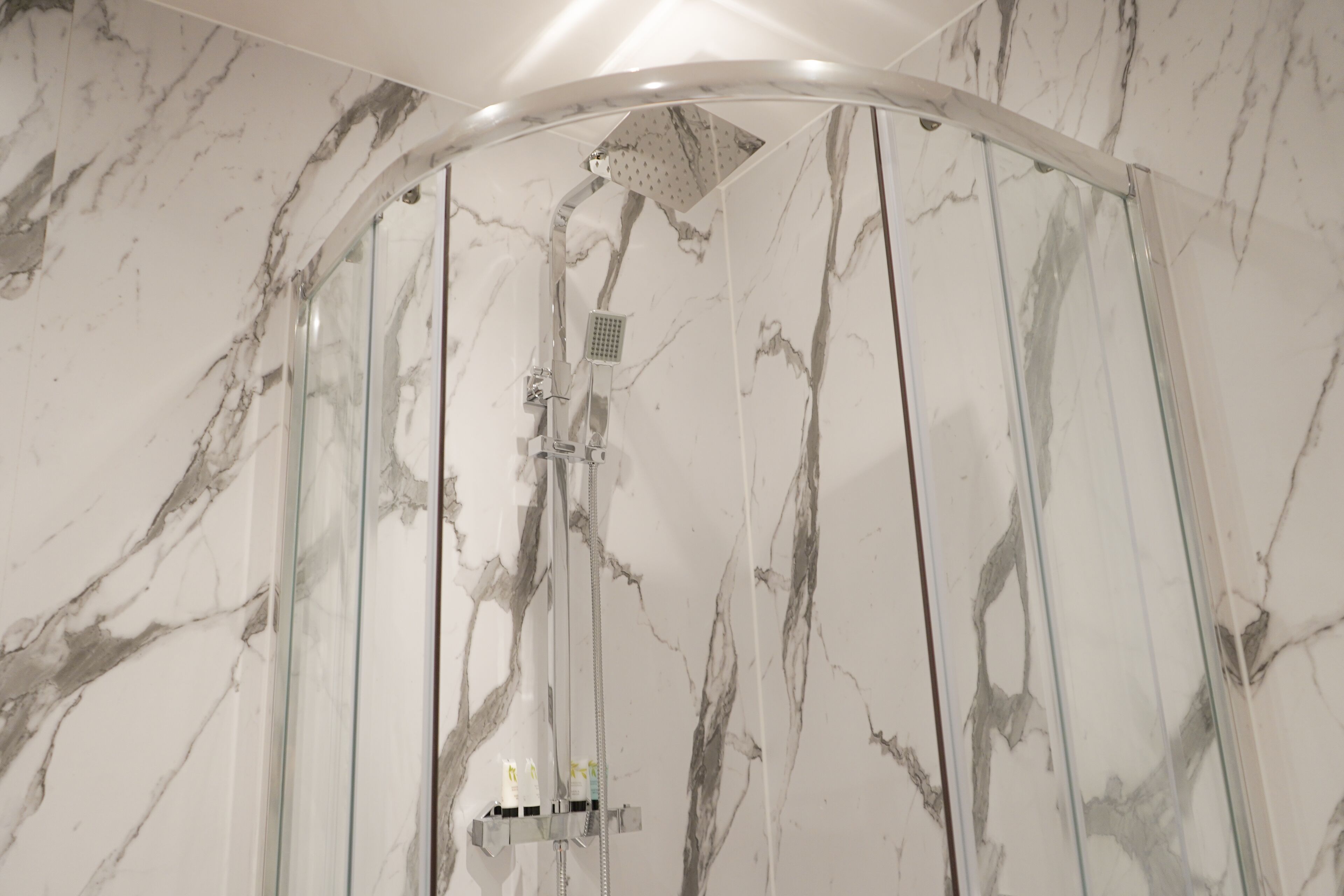Eine Dusche mit Glastrennwand und Marmorwand.
