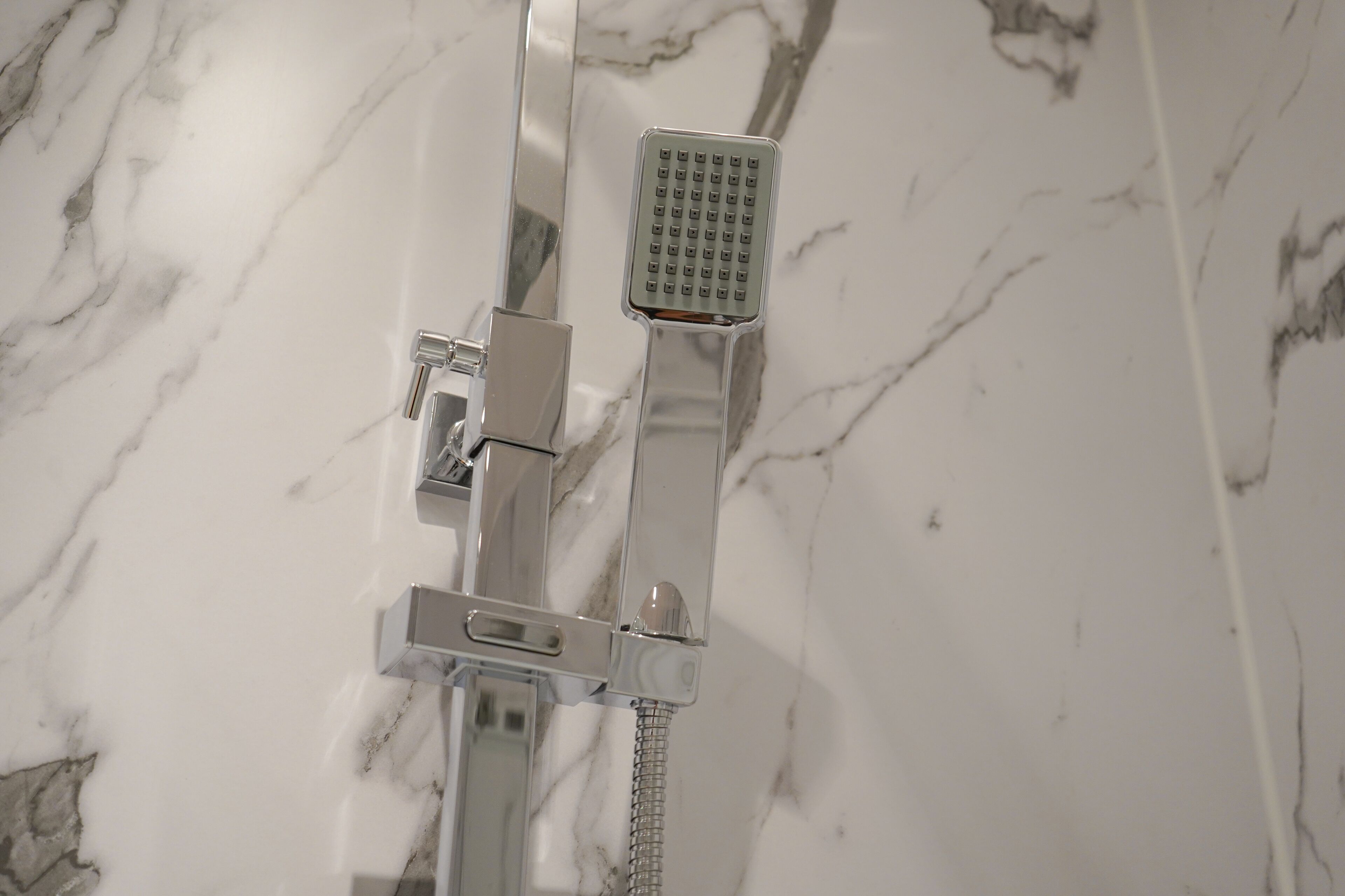 A shower with a handheld showerhead and a fixed showerhead mounted on a wall with a marble-like tile backsplash.