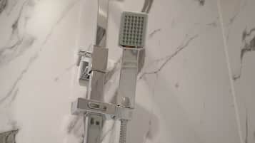 A shower with a handheld showerhead and a fixed showerhead mounted on a wall with a marble-like tile backsplash.