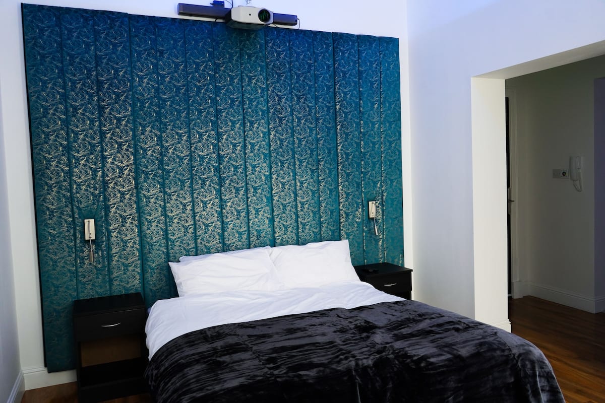 Un dormitorio con cabecera estampada, cama con ropa de cama blanca y una manta negra.
