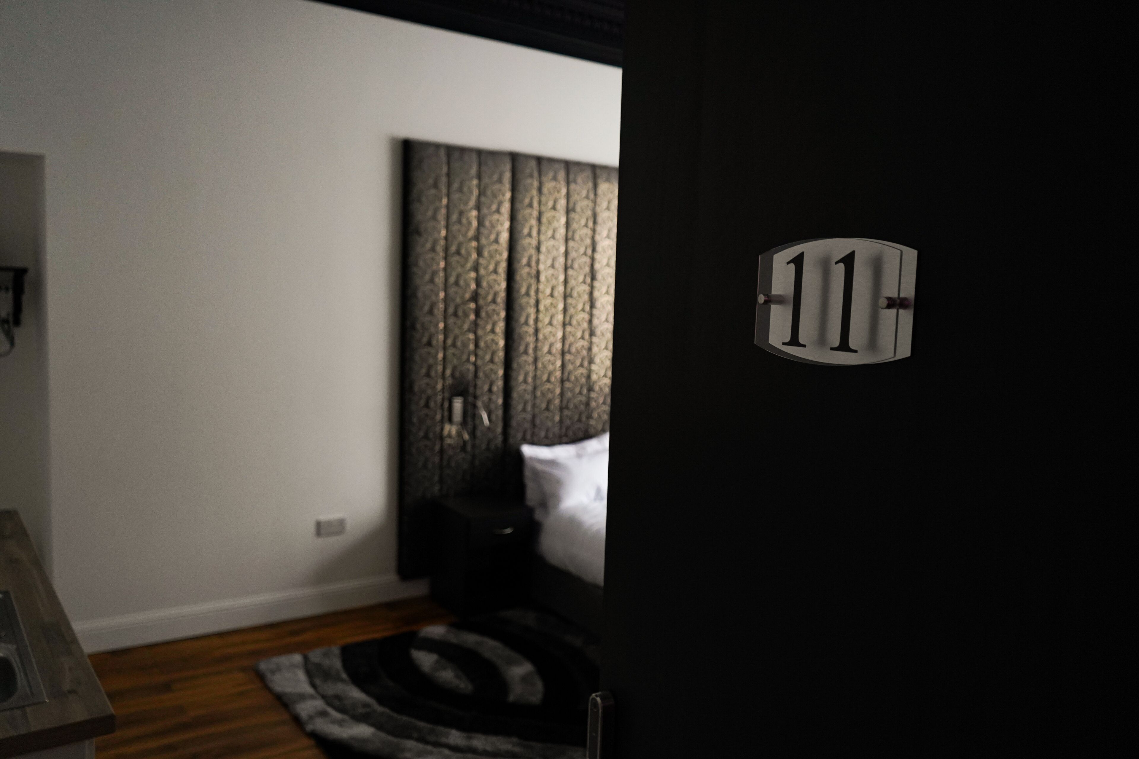 A bedroom with a bed, a nightstand, a rug, and a door with a number.