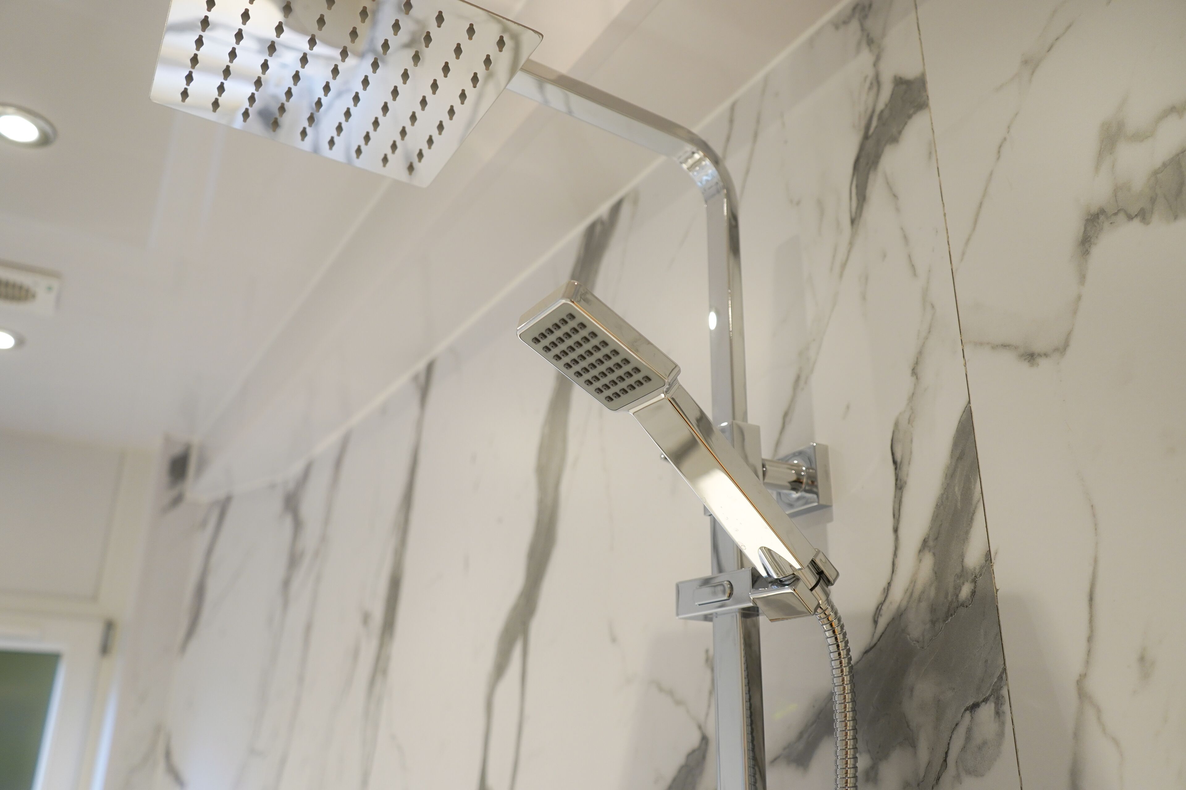 Une douche équipée d’un pommeau de douche à main et d’un pommeau de douche fixe fixé au mur, le tout dans un décor de marbre.
