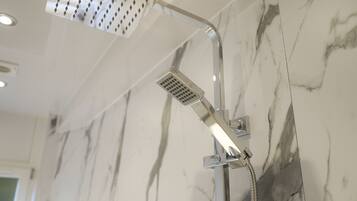 Une douche équipée d’un pommeau de douche à main et d’un pommeau de douche fixe fixé au mur, le tout dans un décor de marbre.