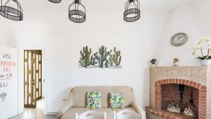 A cozy living room with a beige sofa, two cactus-themed cushions, a wooden coffee table, a brick fireplace, and a whiteboard with motivational writing. - Villetta Sea Sunset by BarbarHouse (Specchiarica)