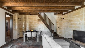 Een rustiek interieur met zichtbare stenen muren, een houten plafond, een eethoek met tafel en stoelen, en een moderne bank.