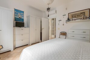 A bedroom with a bed, a wardrobe, a television, and a painting on the wall.