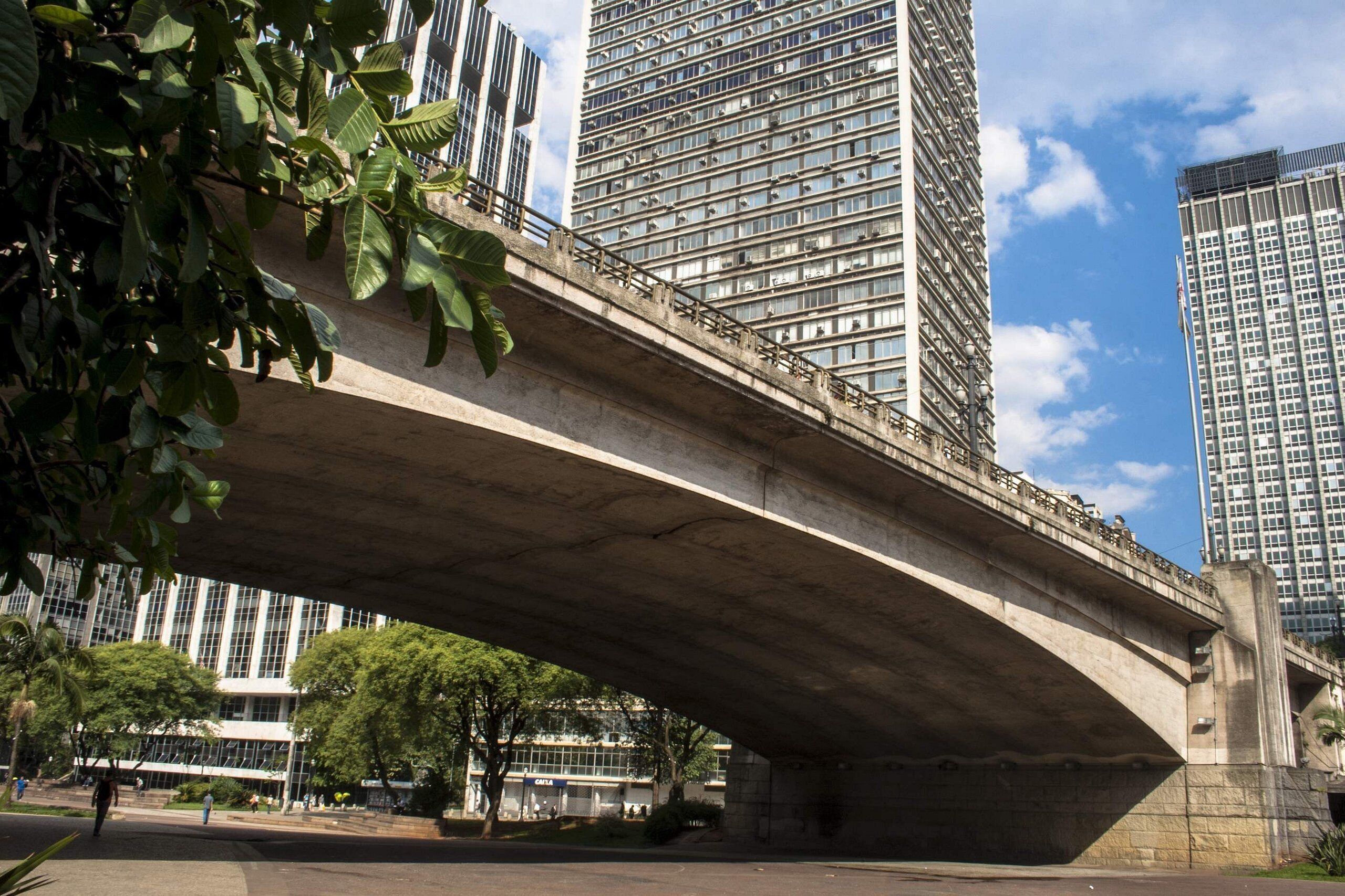A concrete bridge over a road with tall buildings in the background.