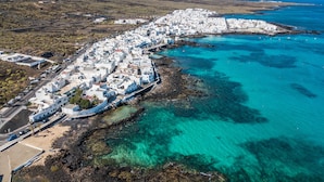 Luchtbeeld van een kustplaatsje met witte gebouwen, helder turquoise water en rotsachtig terrein.