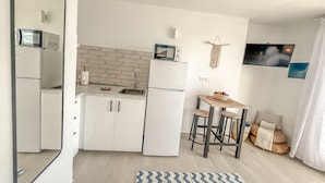 Een kleine keuken met witte kastjes, een magnetron, een koelkast en een eethoekje met krukken.