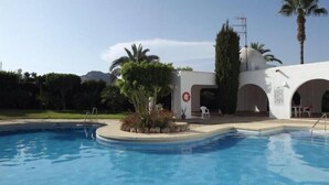 A swimming pool with a curved edge, surrounded by palm trees and a white building with arched doorways.