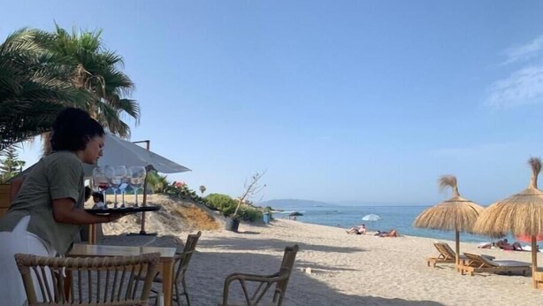 A beachside restaurant with wicker chairs and a table, overlooking the ocean.