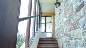 Una escalera con paredes de piedra y escalones de madera que conduce a una habitación con ventanas amplias.