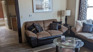 A living room with a brown leather sofa, a glass coffee table, a patterned rug, and a framed picture on the wall. - Hidden Gem in Cortland (Cortland)