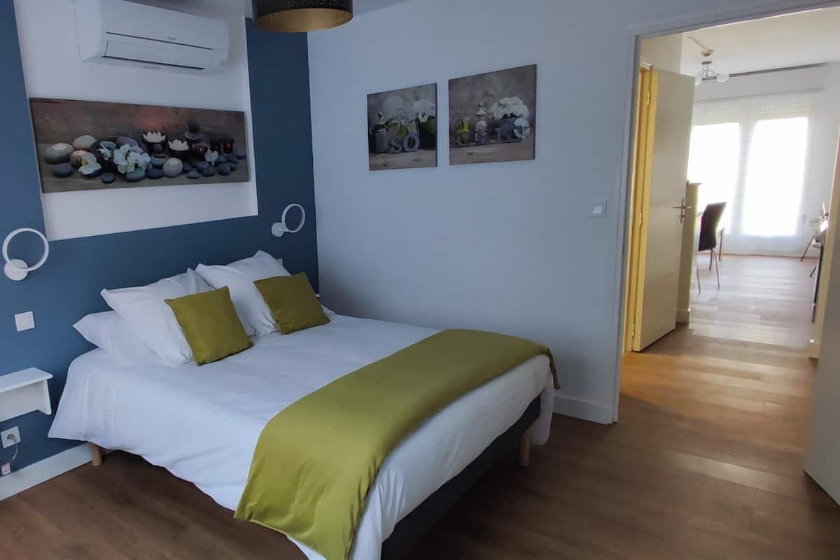 Een slaapkamer met een bed, nachtkastje, lamp en een kunstwerk aan de muur.