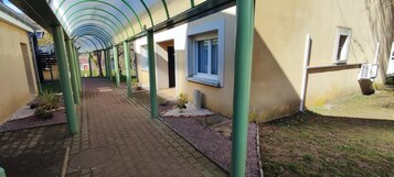 Un pasillo cubierto con suelo de baldosas, pilares verdes y un edificio con ventanas y una puerta.
