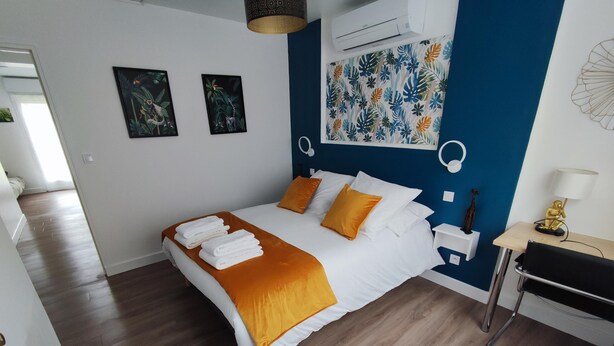 Une chambre moderne avec un lit, une literie blanche et orange, un mur d’accent bleu et un petit bureau avec une lampe.