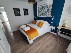 Une chambre moderne avec un lit, une literie blanche et orange, un mur d’accent bleu et un petit bureau avec une lampe.