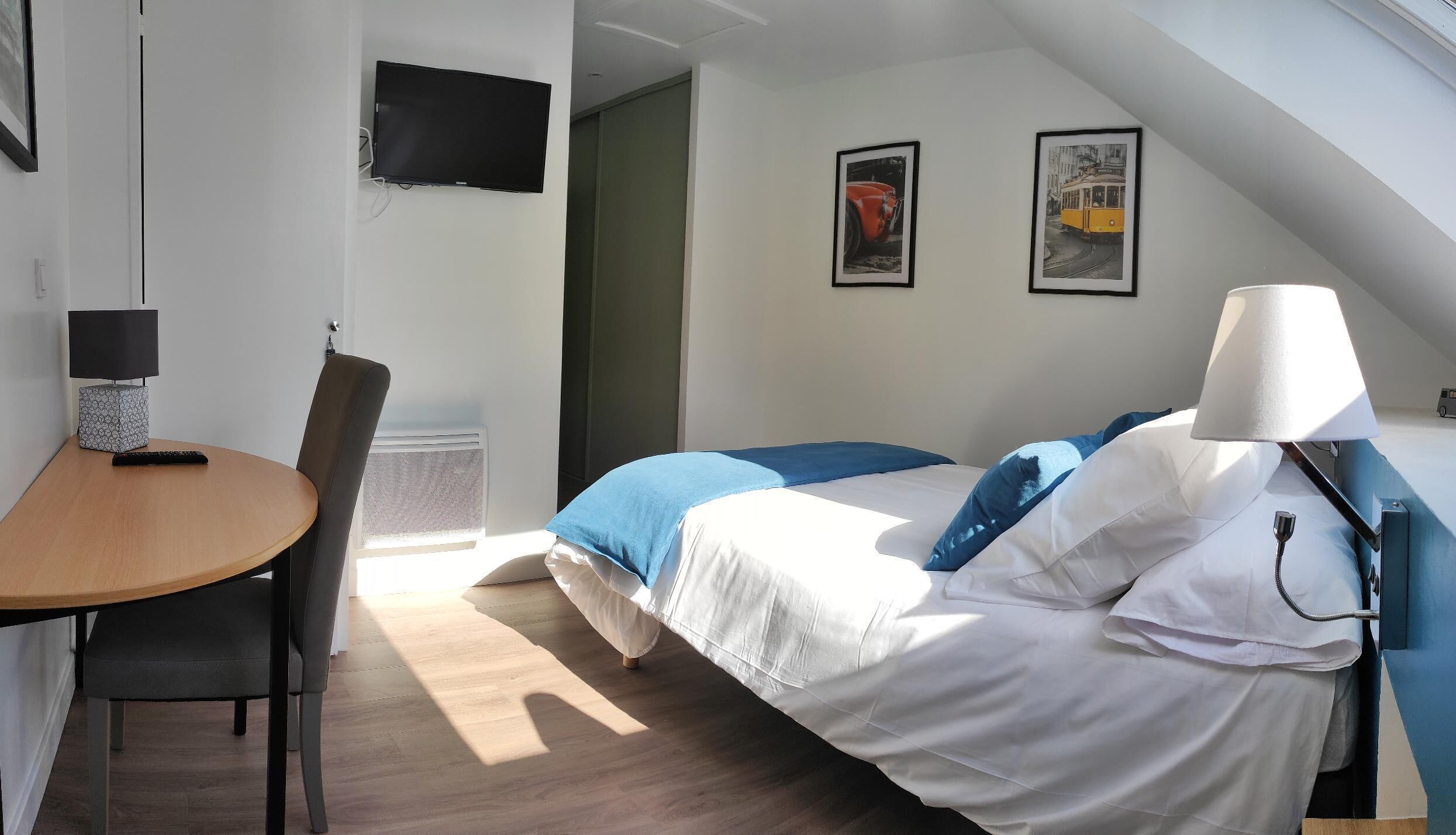 A bedroom with a bed, a desk, a chair, a lamp, and two framed pictures on the wall.