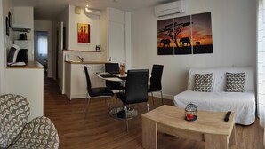 Un salon moderne avec un canapé, une table basse et un coin repas comprenant des chaises et une table. Un tableau représentant des éléphants est accroché au mur.