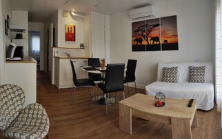 Una sala de estar moderna con sofá, una mesa de centro y un comedor con sillas y una mesa. Hay un cuadro de elefantes en la pared.