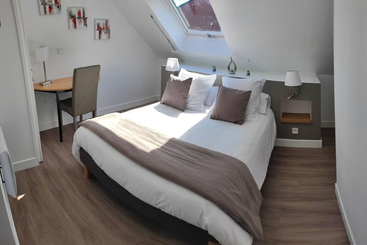 Een slaapkamer met een groot bed, een bureau en een stoel. Boven het bed bevindt zich een dakvenster.