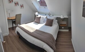 Une chambre avec un grand lit, un bureau et une chaise. Il y a une lucarne au-dessus du lit.