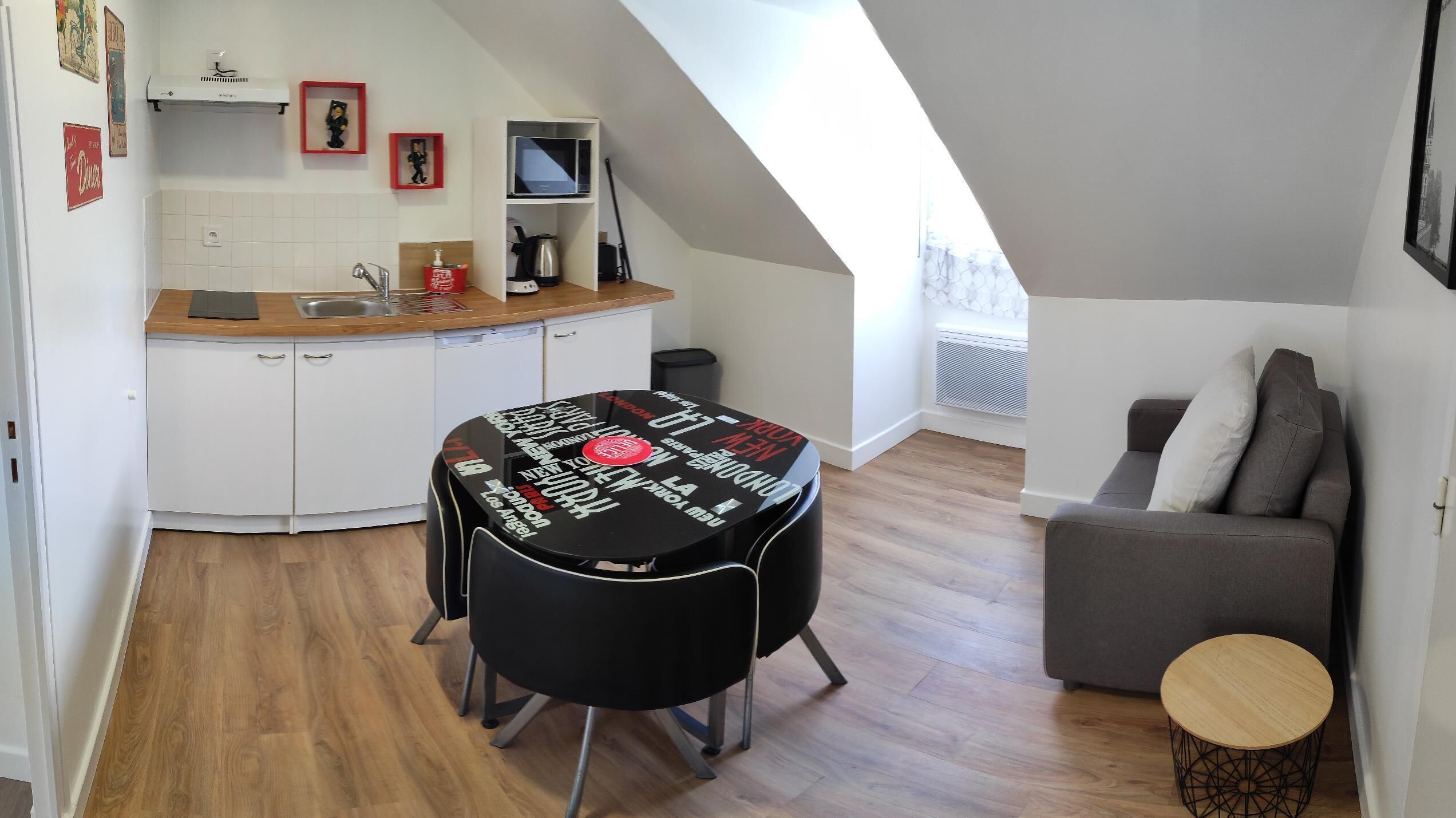 Un espacio habitable compacto con kitchenette, una mesa de comedor con sillas, un sofá y una mesita auxiliar.