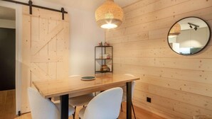 A wooden-paneled room with a dining table, chairs, a hanging light fixture, and a round mirror on the wall. - 190m from ski slopes, 1st floor, balcony, tv, ski locker, 39m², Morzine (Morzine)