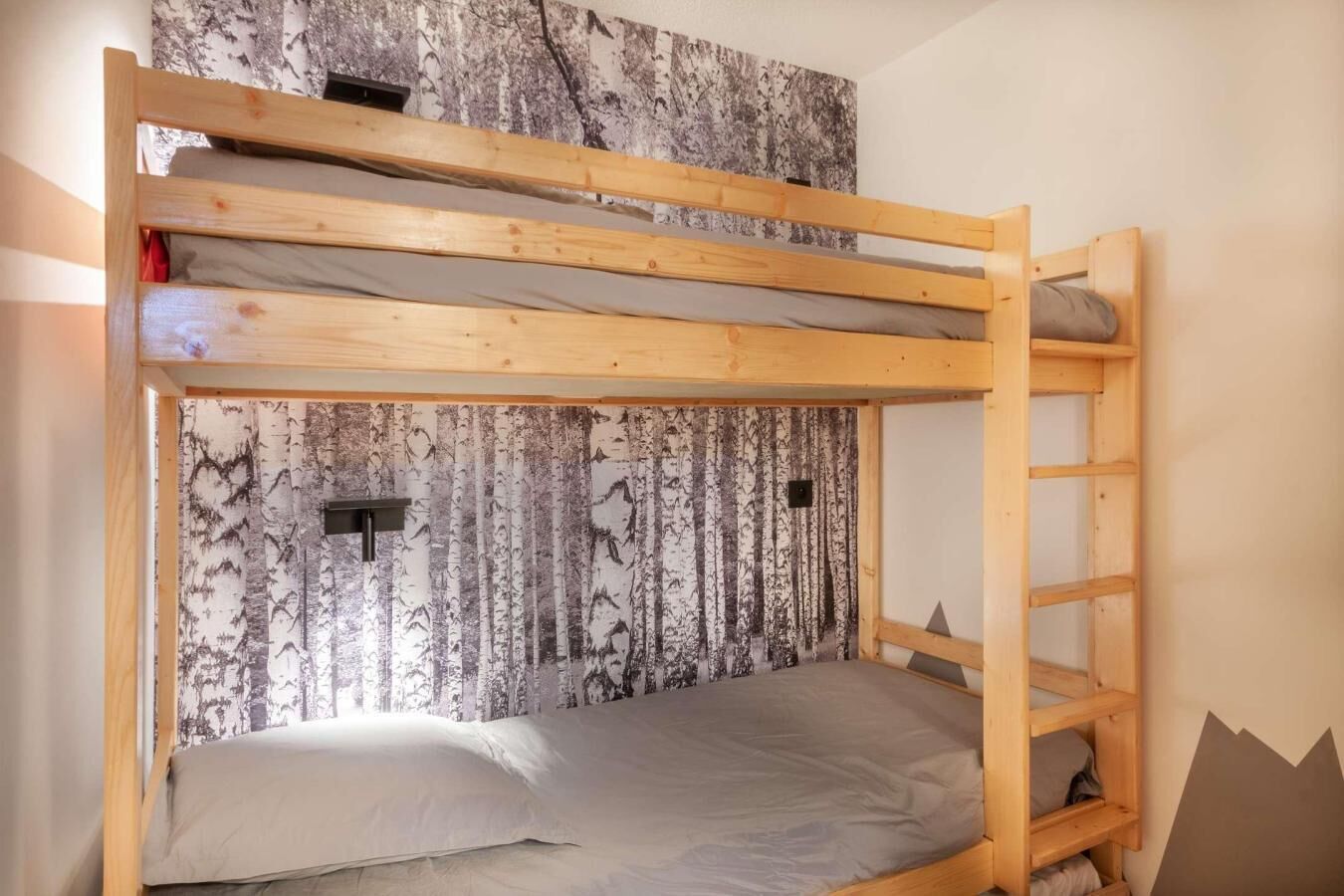 Un lit superposé avec une structure en bois, un matelas et des oreillers. Un mur est décoré d’un motif représentant un bouleau.