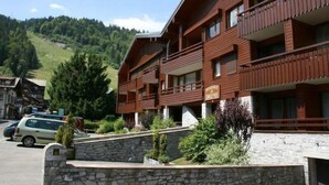 A multi-story hotel with balconies, a stone wall in front, and a mountainous backdrop. - 190m from ski slopes, 1st floor, balcony, tv, ski locker, 39m², Morzine (Morzine)