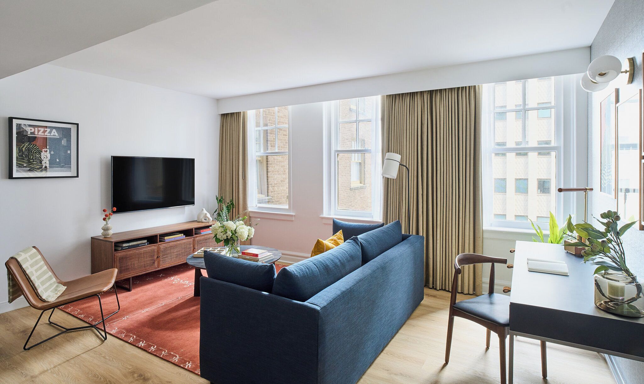 Een moderne woonkamer met een blauwe bank, een televisie, een houten salontafel en een eethoek met een stoel en een plant.
