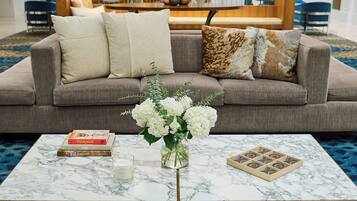 A living room with a grey sofa, a marble coffee table, a vase with white flowers, and a board game.