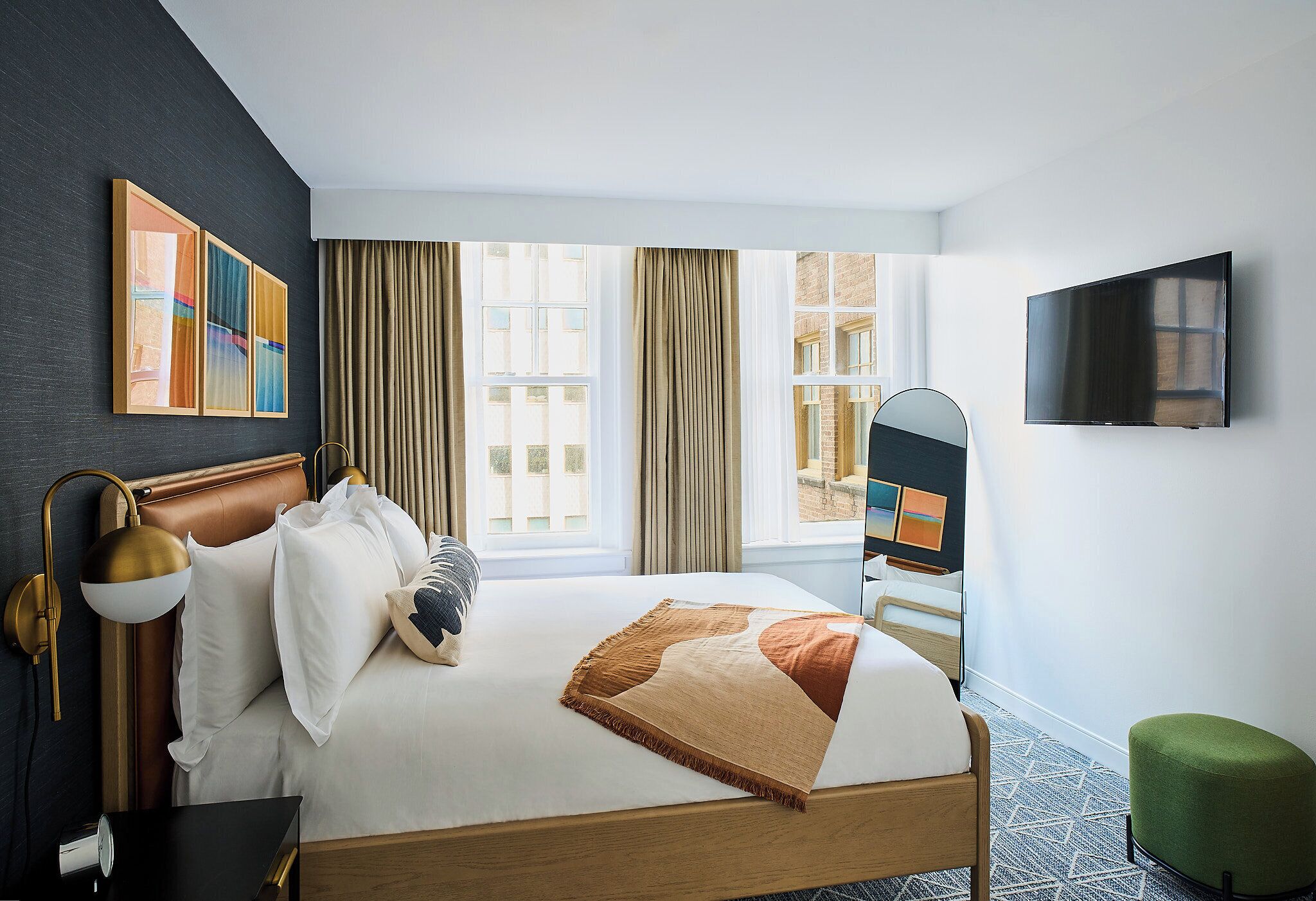 A hotel room with a bed, a TV, a desk, and a green ottoman.