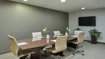 A conference room with a large table, six chairs, and a flat-screen TV on the wall.