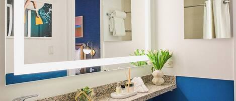 A modern bathroom with a granite countertop, a large mirror, a toilet, and a blue accent wall.