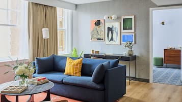 Un salón moderno con un sofá azul, una mesa de centro redonda y una alfombra roja. Hay un escritorio con una lámpara y obras de arte enmarcadas en la pared.