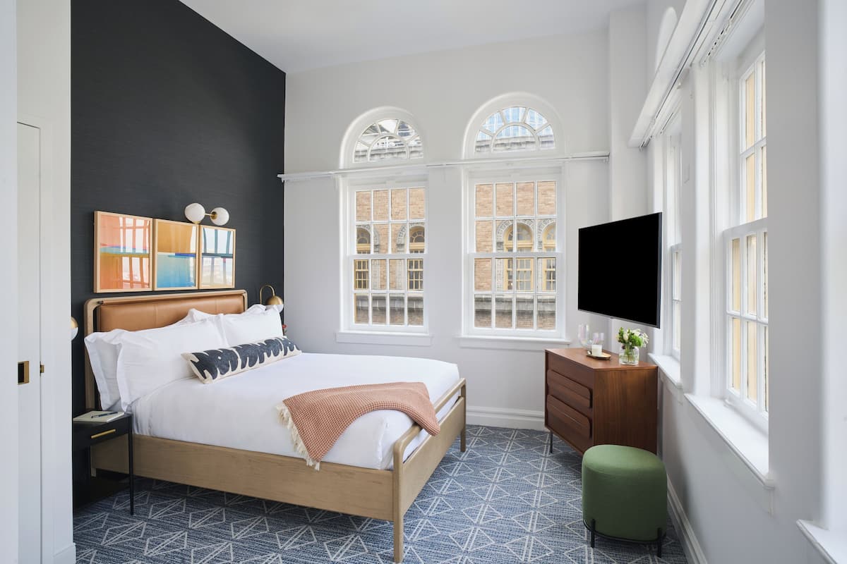 A modern bedroom with a bed, a dresser, a TV, and two windows with arched tops.