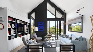 A modern living room with a high ceiling, a large TV, a sofa, and a bookshelf. - Superbe Villa Piscine Intérieure (Combrit)