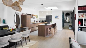 A modern kitchen with a central island, bar stools, and pendant lighting. - Superbe Villa Piscine Intérieure (Combrit)