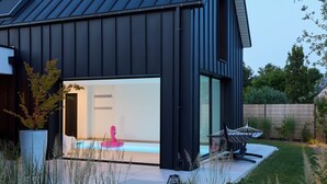 A modern house with a dark exterior, a visible swimming pool, and a well-maintained garden. - Superbe Villa Piscine Intérieure (Combrit)