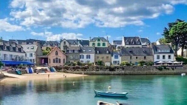 A coastal village with traditional buildings, a sandy beach, and several small boats anchored in calm waters. - Superbe Villa Piscine Intérieure (Combrit)