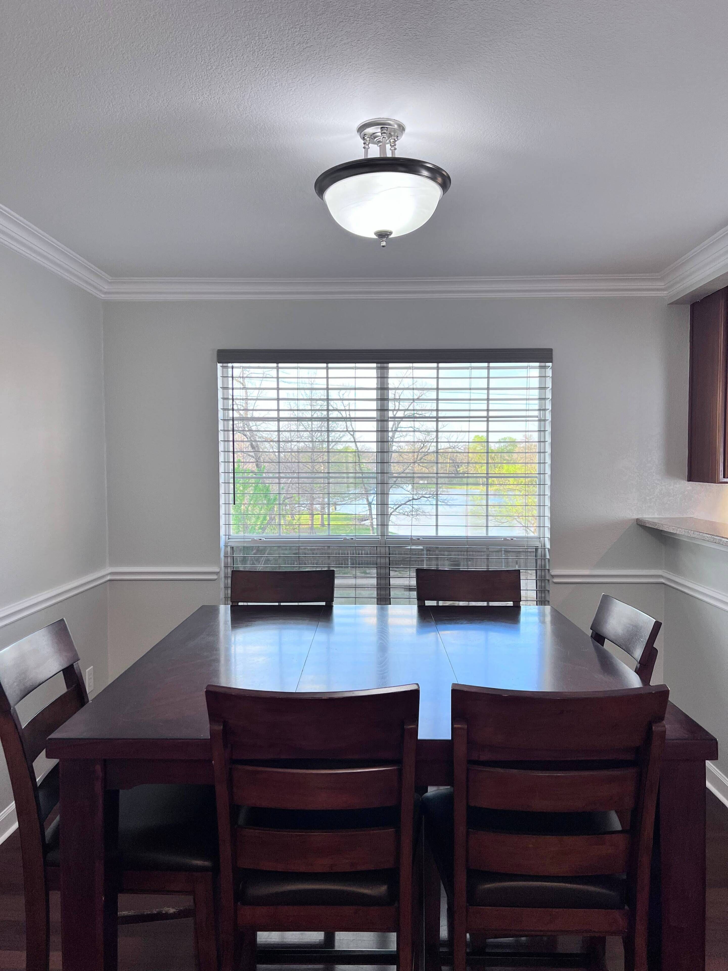 A dining room with a large table and four chairs, a ceiling fan, and a window with blinds.