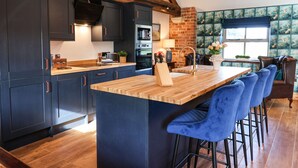 A modern kitchen with dark cabinets, a wooden island, and blue bar stools. - Beth's Cottage (Malton)
