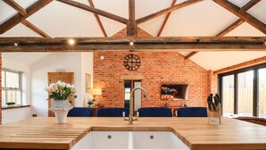 A kitchen with a large sink, wooden beams, a brick wall, and a dining area with blue chairs. - Beth's Cottage (Malton)