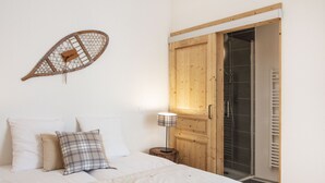 A bedroom with a bed, pillows, a wall-mounted decorative item, a wooden door, and a shower area. - TERRESENS - Les Edelweiss (Vaujany)