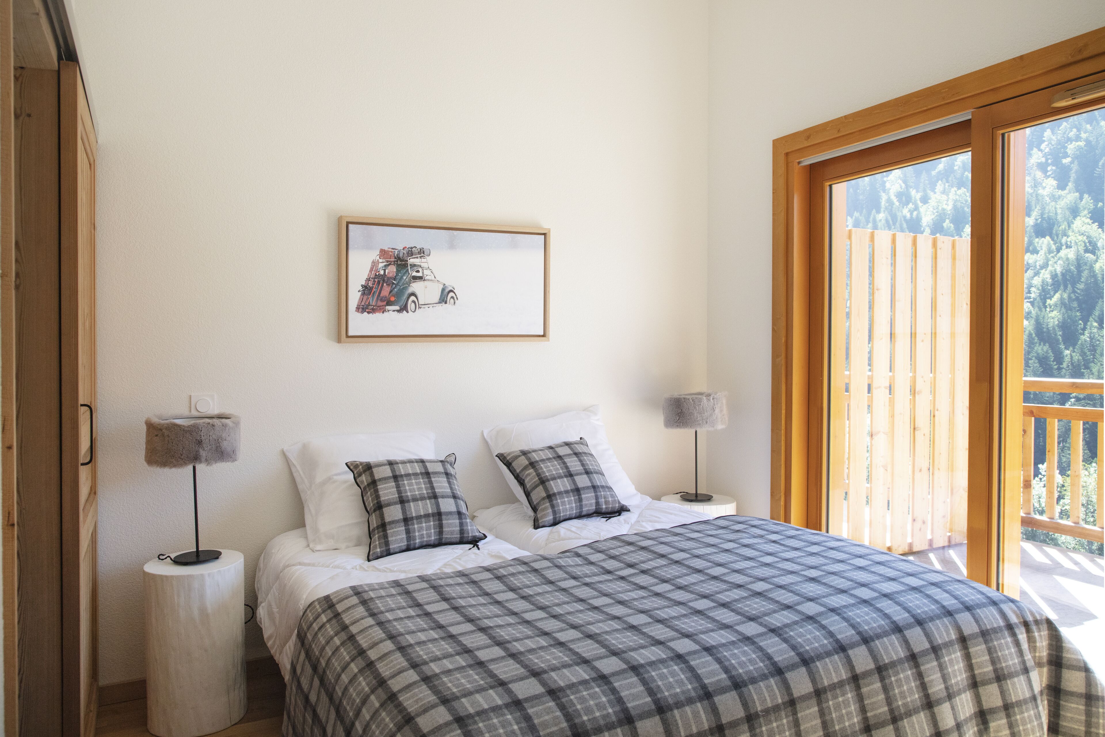 Ein Schlafzimmer mit einem Bett, zwei Nachttischen, einem gerahmten Bild an der Wand und einem großen Fenster mit Blick auf Bäume.