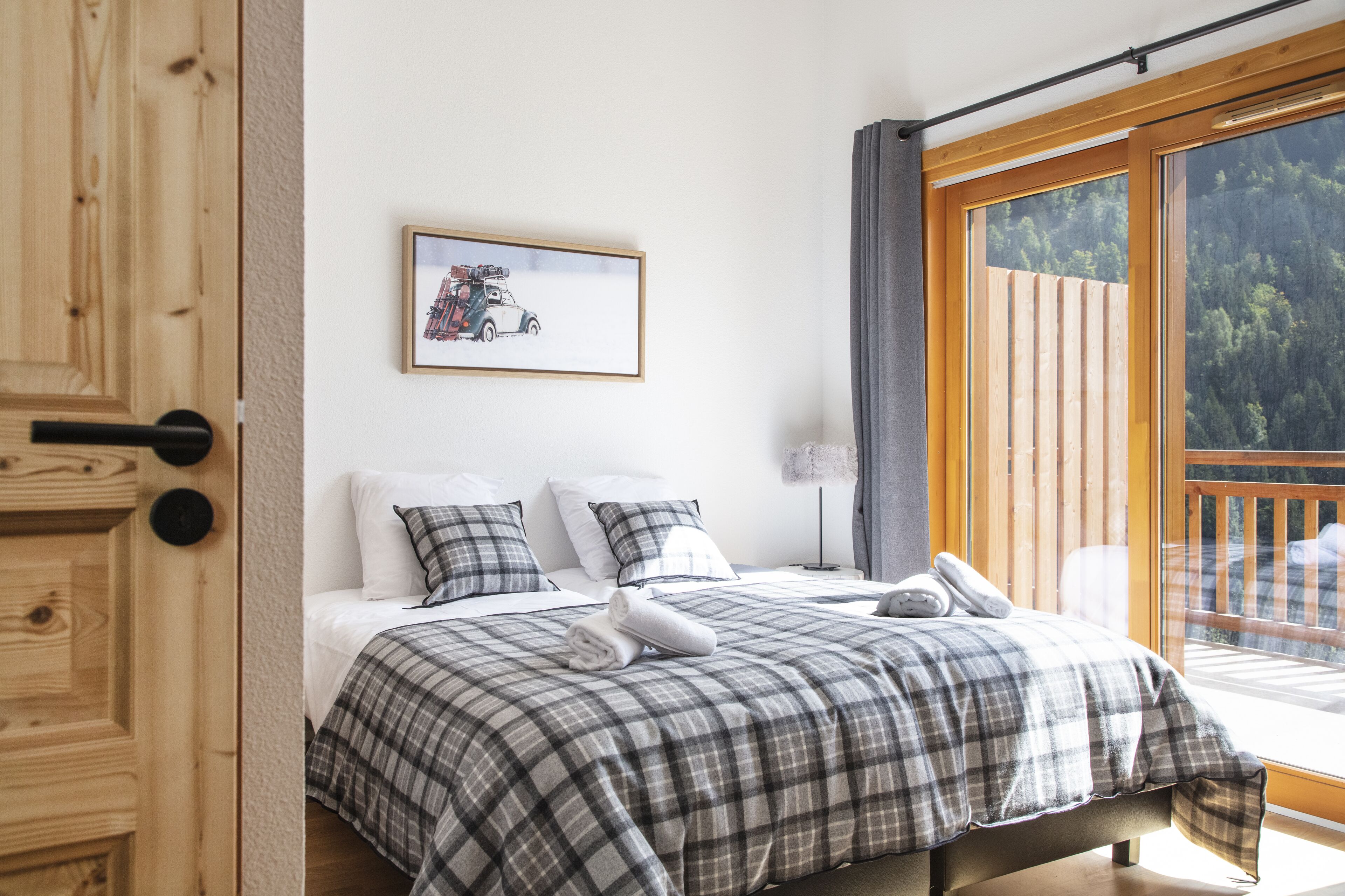 A bedroom with a large bed, a framed picture on the wall, and a view of a balcony with a wooden railing.